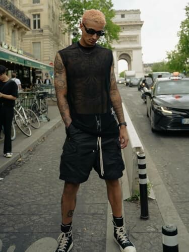 Person with tattoos wearing a black sleeveless shirt and shorts on a Paris street.