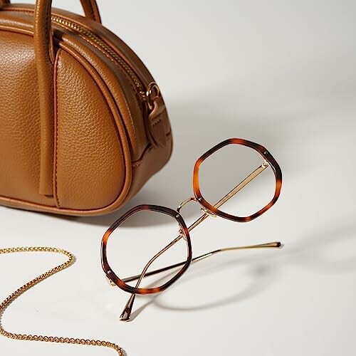 Brown leather handbag and geometric glasses on white background.