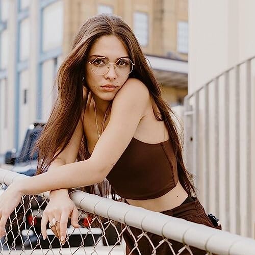 Woman with long hair and glasses leaning on a fence